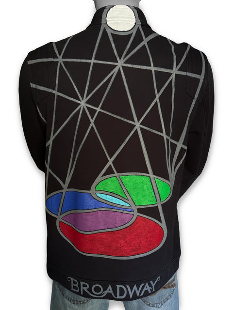 Black long-sleeve jacket shown from the back on a mannequin, featuring a painted geometric gray line pattern across the upper back and a stained-glass style multicolor abstract design near the lower back. BROADWAY is painted in gray at the bottom hem.