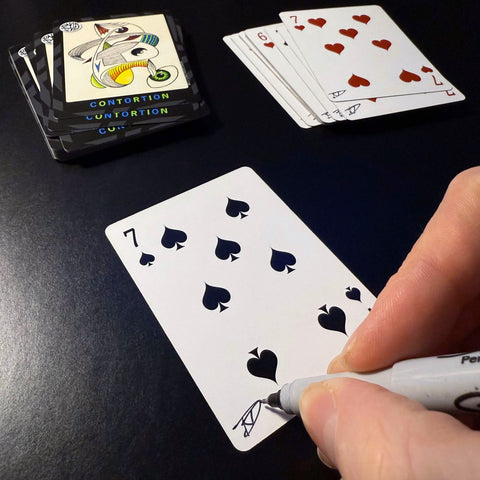 Back of the playing card showing the 7 of spades with a hand‑signed signature ‘DJ’ in black ink.