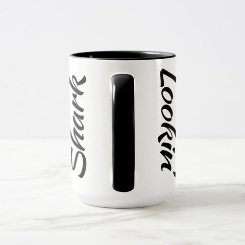 White ceramic coffee mug with a black handle and black interior, featuring a wrap‑around print of the artwork titled “Lookin’ Shark.“