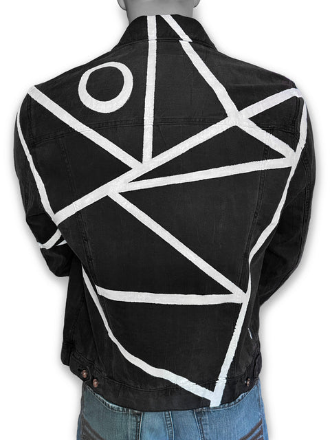 A black denim jacket with a bold white geometric line pattern and a white circle motif on the back, shown on a mannequin from the rear.