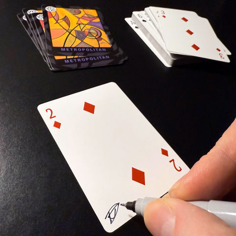Back of the playing card showing the 2 of diamonds with a hand‑signed signature ‘DJ’ in black ink.