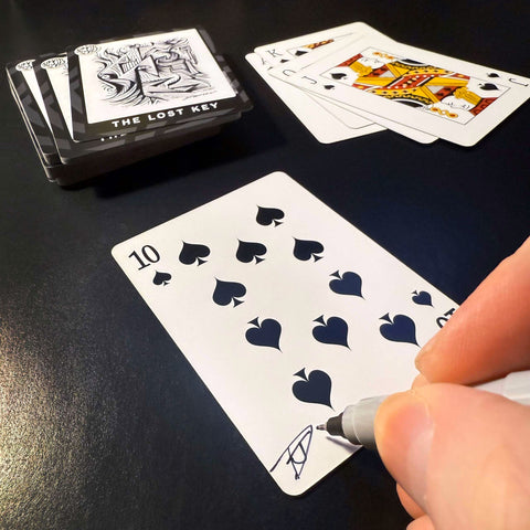 Back of the playing card showing the 10 of spades with a hand‑signed signature ‘DJ’ in black ink.