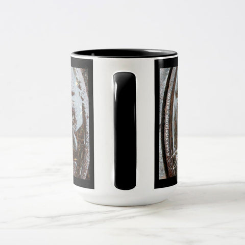 A white ceramic coffee mug with a black handle and black interior, focusing on the handle, with the beginning and end sections of a wrap-around photographic print of a wet street plate with the word ‘WATER’.