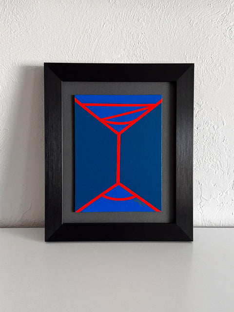 An abstract geometric painting featuring a minimalist red line design of a martini-like glass on a two-toned blue background; signed 'DARIN' in lower right; mounted on a gray mat and framed in black, atop a white shelf, against a white textured wall.