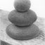A black and white graphite drawing of three stacked rounded stones, as a cairn, on a wood surface, with a visible artist signature ‘Darin’ near the bottom right.