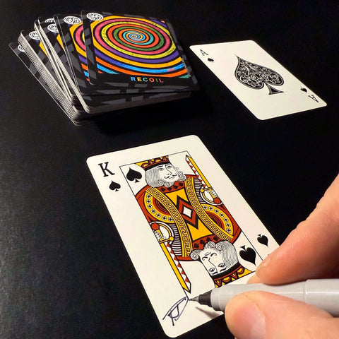 Back of the playing card showing the King of spades with a hand‑signed signature ‘DJ’ in black ink.