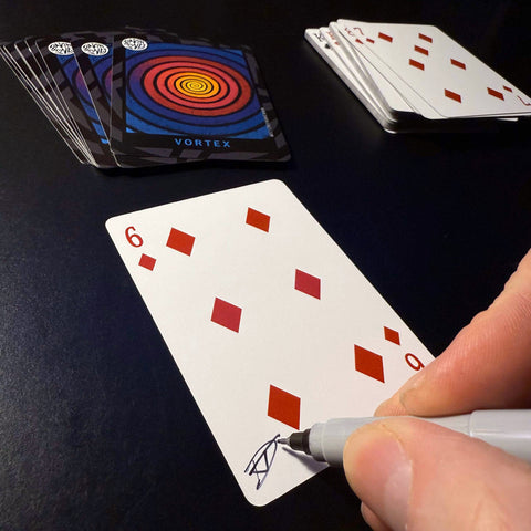 Back of the playing card showing the 6 of diamonds with a hand‑signed signature ‘DJ’ in black ink.