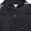 Close-up of a black Calvin Klein zip-up jacket with a high collar, two snap buttons, and a zippered chest pocket, showing a white brand label inside the collar and painted lines on the shoulders.