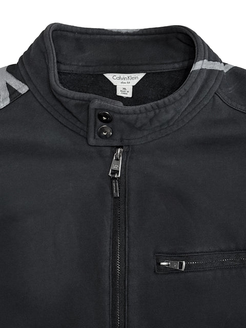 Close-up of a black Calvin Klein zip-up jacket with a high collar, two snap buttons, and a zippered chest pocket, showing a white brand label inside the collar and painted lines on the shoulders.
