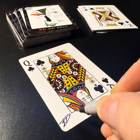 Back of the playing card showing the Queen of clubs with a hand‑signed signature ‘DJ’ in black ink.