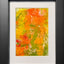 Abstract textured painting with layered brush and palette-knife strokes in orange, yellow, and green; matted in white and framed in black.