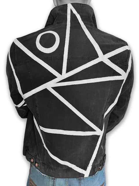 A black denim jacket with a bold white geometric line pattern and a white circle motif on the back, shown on a mannequin from the rear, with the collar up.