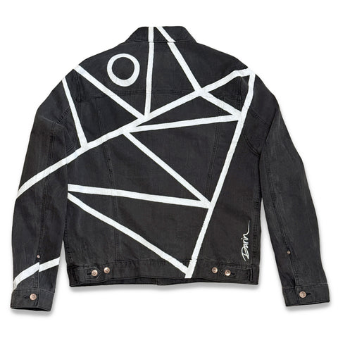A black denim jacket shown from the back, featuring a bold, painted, white geometric line design and a white circular motif on the upper back, with the signature Darin near the lower right side.