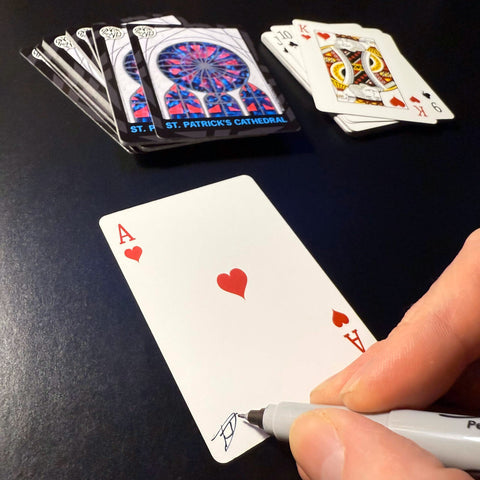 Back of the playing card showing the Ace of hearts with a hand‑signed signature ‘DJ’ in black ink.