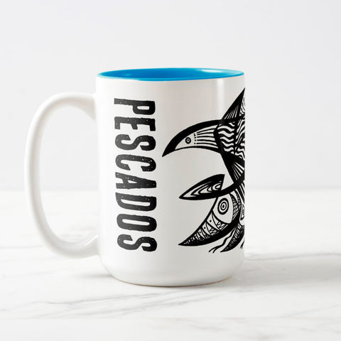White ceramic coffee mug with a white handle and blue interior, featuring a wrap‑around print of the artwork titled “Pescados.“