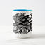 White ceramic coffee mug with a white handle and blue interior, featuring a wrap‑around print of the artwork titled “Pescados.“