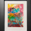 Abstract textured painting with layered brush and palette-knife strokes in pink, turquoise, yellow, orange, green, red, and black; matted in white and framed in black.