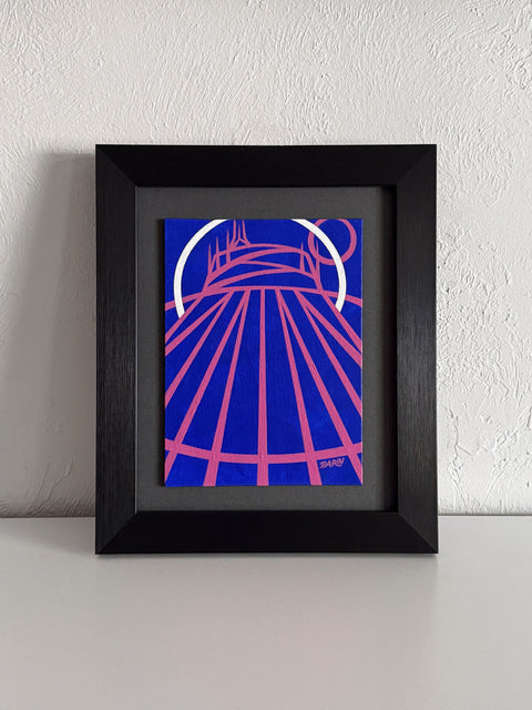 A stylized abstract painting of a tent-like structure with radiating pink lines and a white arc on a vivid blue background; signed 'DARIN' in the lower-right, mounted on a gray mat and framed in black, atop a white shelf, against a white textured wall. 