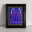 A stylized abstract painting of a tent-like structure with radiating pink lines and a white arc on a vivid blue background; signed 'DARIN' in the lower-right, mounted on a gray mat and framed in black, atop a white shelf, against a white textured wall. 