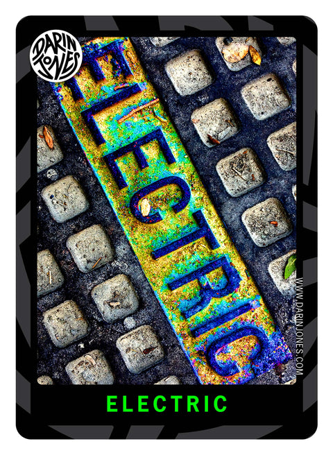 A photograph of a waffle-pattern metal street plate with the word 'ELECTRIC' in bright blue, green, and yellow and the same text title at the bottom in bright green, and a black and gray design border, the DARIN JONES logo in the upper left, and website on the right.