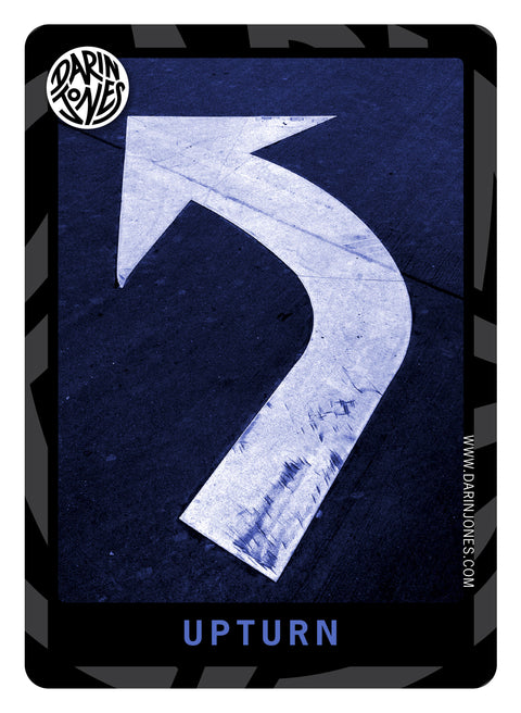 A photograph featuring a large white curved arrow painted on a dark navy asphalt-like surface, with the word 'UPTURN' at the bottom, a black and gray design border, the DARIN JONES logo in the upper left, and website on the right.