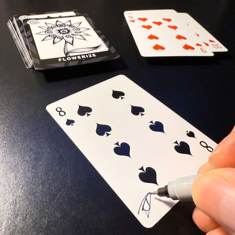 Back of the playing card showing the 8 of spades with a hand‑signed signature ‘DJ’ in black ink.