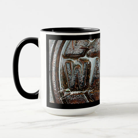 A white ceramic coffee mug with a black handle and black interior, featuring the ‘WA’ section of a wrap-around photographic print of a wet street plate with the word ‘WATER’. 