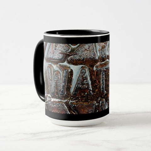 A white ceramic coffee mug with a black handle and black interior, featuring the ‘WAT’ section of a wrap-around photographic print of a wet street plate with the word ‘WATER’. 