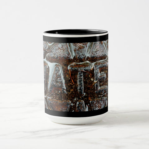 A white ceramic coffee mug with a black handle and black interior, featuring the ‘ATE’ section of a wrap-around photographic print of a wet street plate with the word ‘WATER’. 
