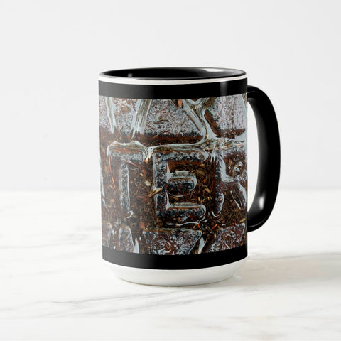 A white ceramic coffee mug with a black handle and black interior, featuring the ‘TER’ section of a wrap-around photographic print of a wet street plate with the word ‘WATER’. 