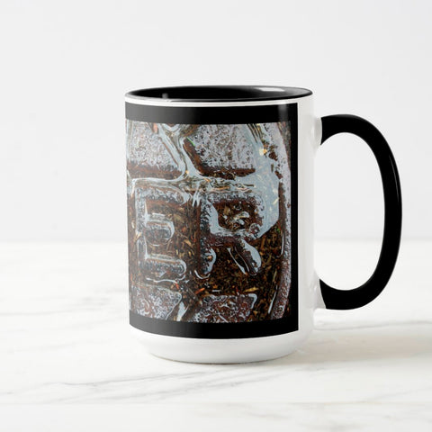 A white ceramic coffee mug with a black handle and black interior, featuring the ‘ER’ section of a wrap-around photographic print of a wet street plate with the word ‘WATER’. 