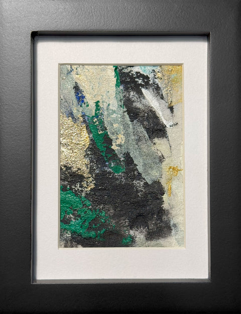 Abstract textured painting with layered brush and palette knife strokes in black, gray, off-white, metallic gold, and green; matted in white and framed in black.