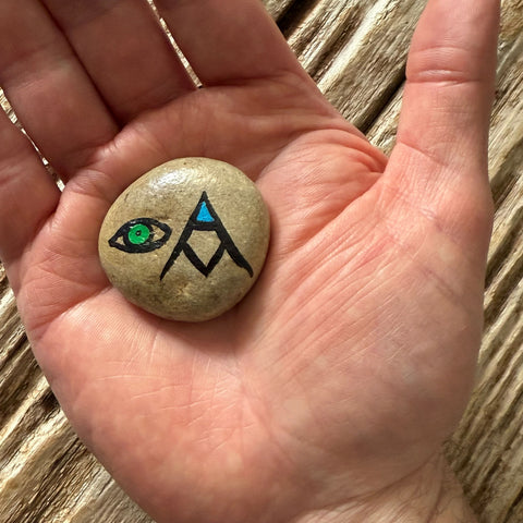 A green eye outlined in black and a stacked AM in the form of a mountain with blue inside the A, resting in a person’s palm.