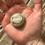 Hand‑painted stone with the word ‘WONDER’ in white within a black oval outline and metallic gold accent, resting in a person’s palm.