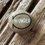 Hand‑painted stone with the word ‘WONDER’ in white within a black oval outline and metallic gold accent, placed on a textured wooden surface.