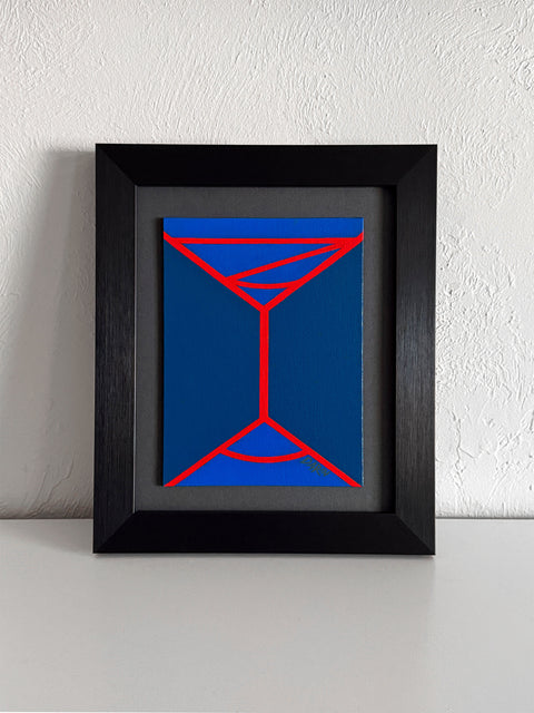 An abstract geometric painting featuring a minimalist red line design of a martini-like glass on a two-toned blue background; signed 'DARIN' in lower right; mounted on a gray mat and framed in black, atop a white shelf, against a white textured wall.